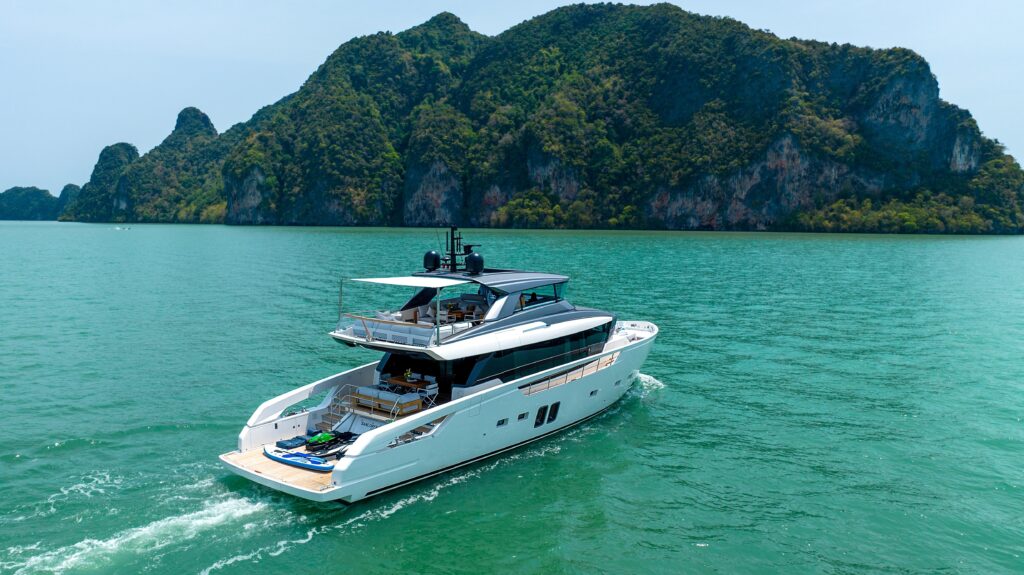 2023 Sanlorenzo SX76 yacht cruising in turquoise waters near lush green islands.