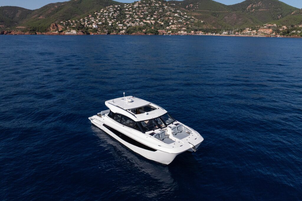 Aquila 42 Coupe 2025 yacht cruising on serene blue waters near a coastal landscape.