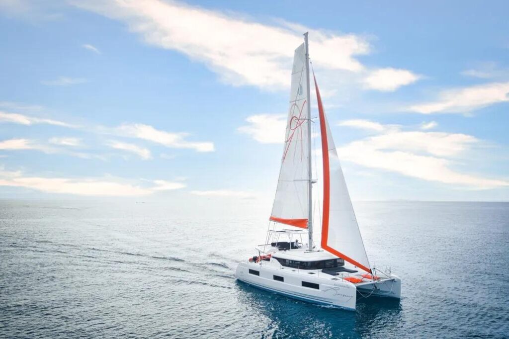 2020 Lagoon 46 catamaran sailing on open sea under clear blue sky.
