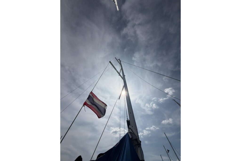 Thai flag waving on a sailboat mast against a cloudy sky.