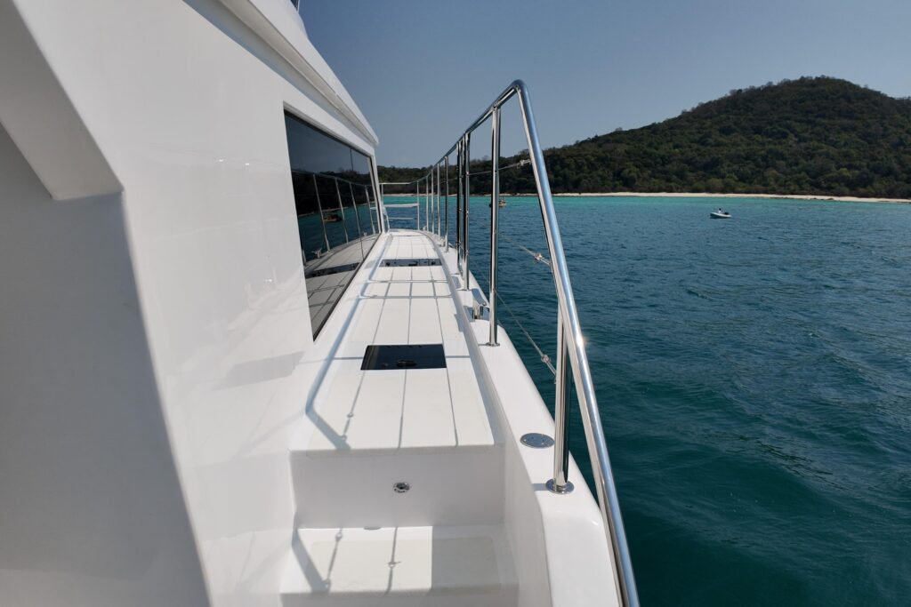 Yacht deck with stainless steel railing overlooking turquoise water and a tropical island.