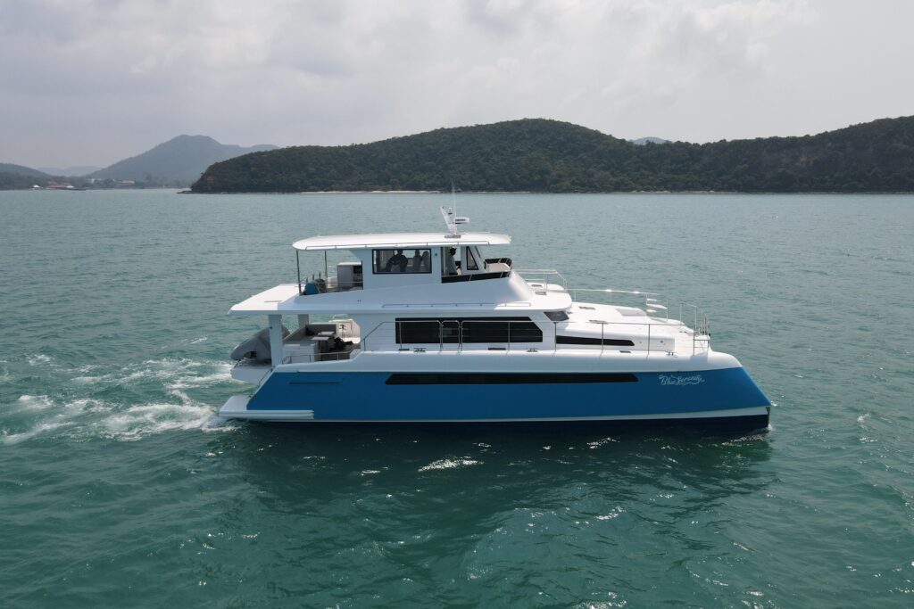 Luxury catamaran yacht sailing on turquoise water with green island backdrop.
