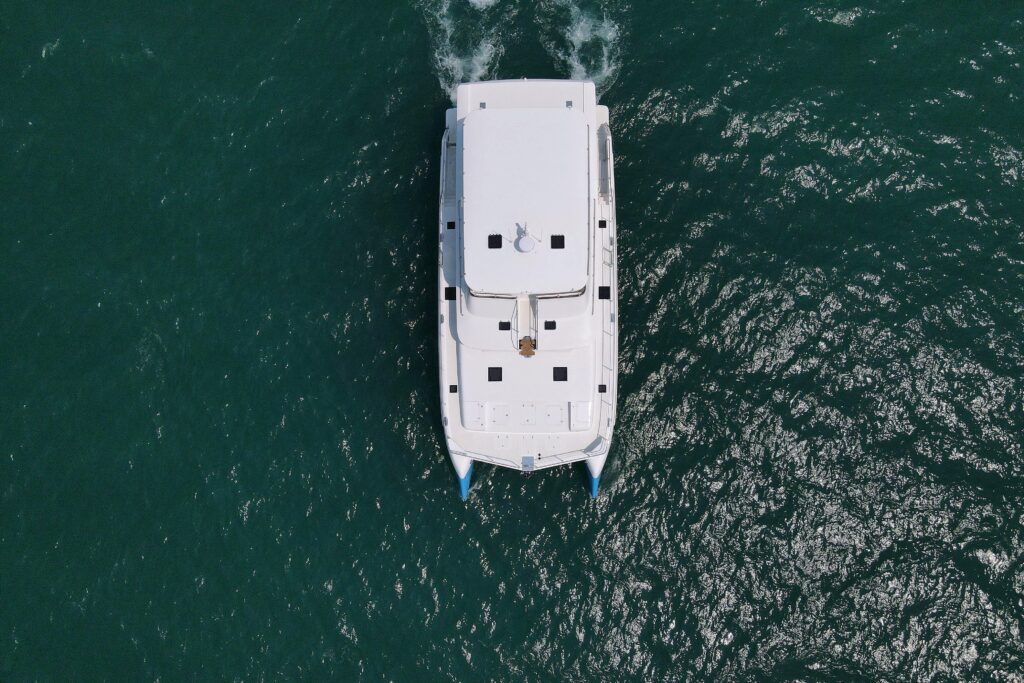 Aerial view of a white catamaran sailing on deep green water.